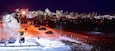 A snowy parking lot with cars and a city skyline in the background.