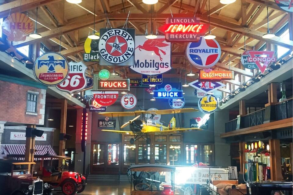 A vintage car showroom with various classic cars and a display of old trucks.