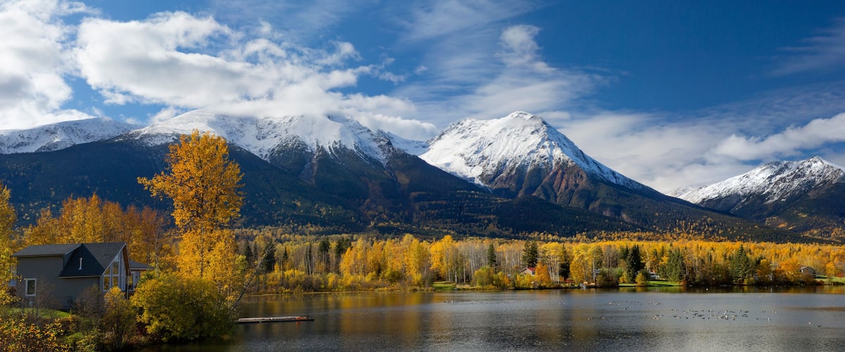 A lake surrounded by autumn-colored trees and snow-capped mountains.