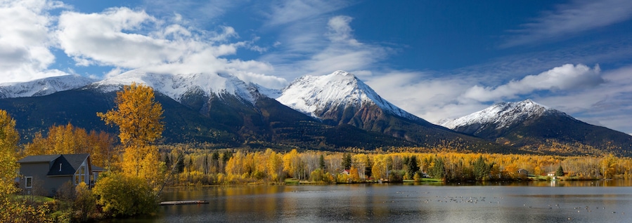Un lago rodeado de árboles con colores otoñales y montañas nevadas.