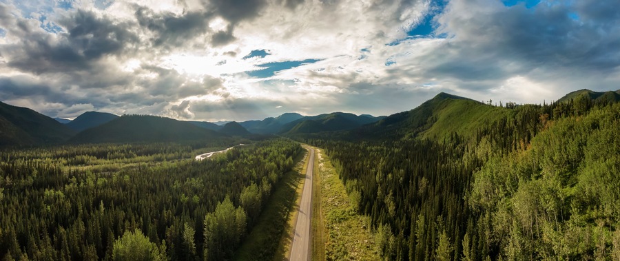 Beautiful Panoramic View of Scenic Road from Above surrounded by Lush Forest and Mountains. Aerial Drone Shot. Alaska Highway, West of Fort Nelson. Northern Rockies, British Columbia, Canada.