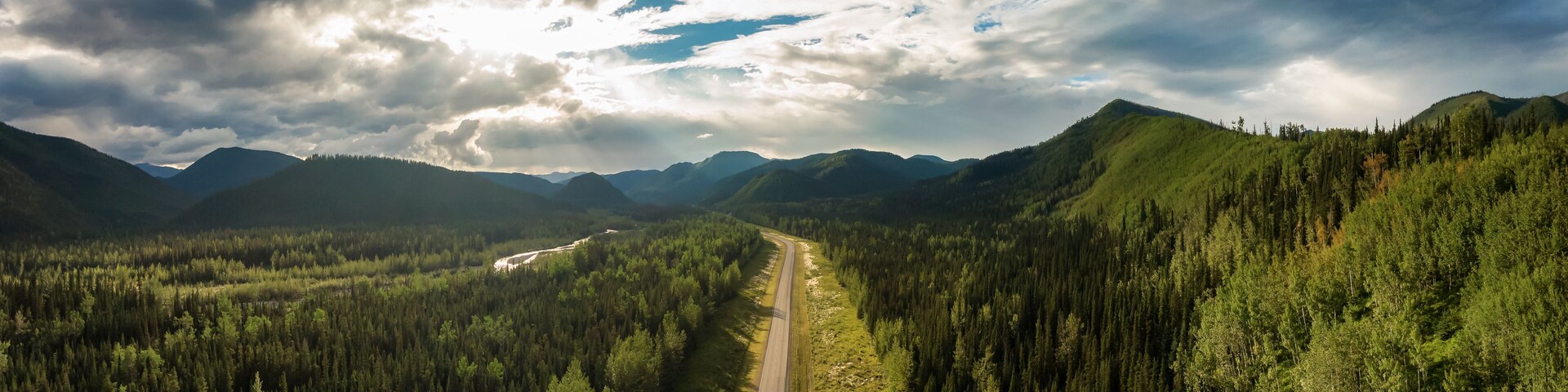 Beautiful Panoramic View of Scenic Road from Above surrounded by Lush Forest and Mountains. Aerial Drone Shot. Alaska Highway, West of Fort Nelson. Northern Rockies, British Columbia, Canada.