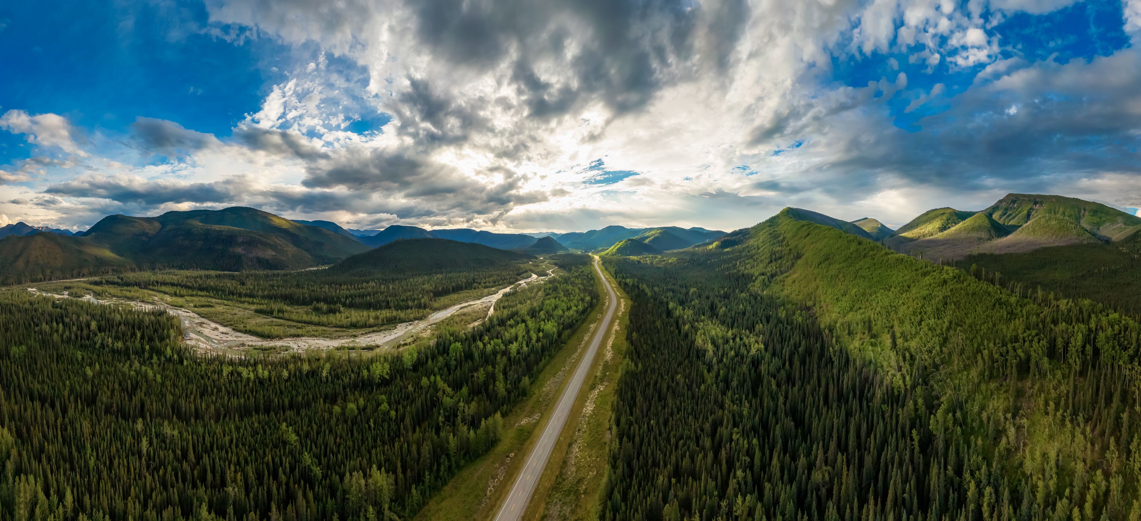Beautiful Panoramic View of Scenic Road from Above surrounded by Lush Forest and Mountains. Aerial Drone Shot. Alaska Highway, West of Fort Nelson. Northern Rockies, British Columbia, Canada.