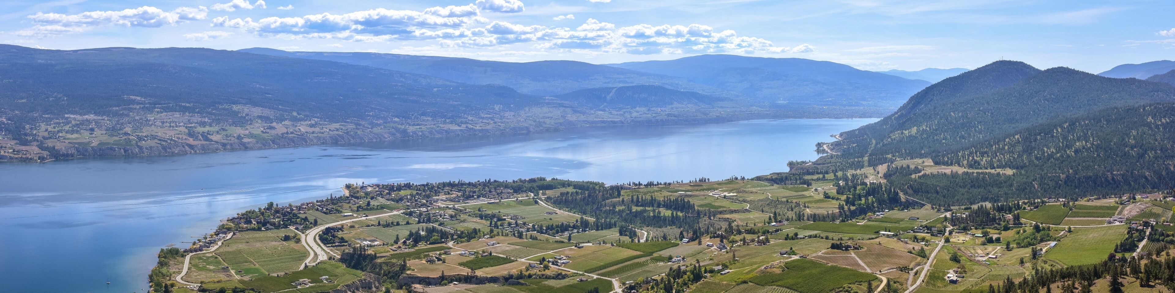 A lake surrounded by mountains and a small town with fields and roads.