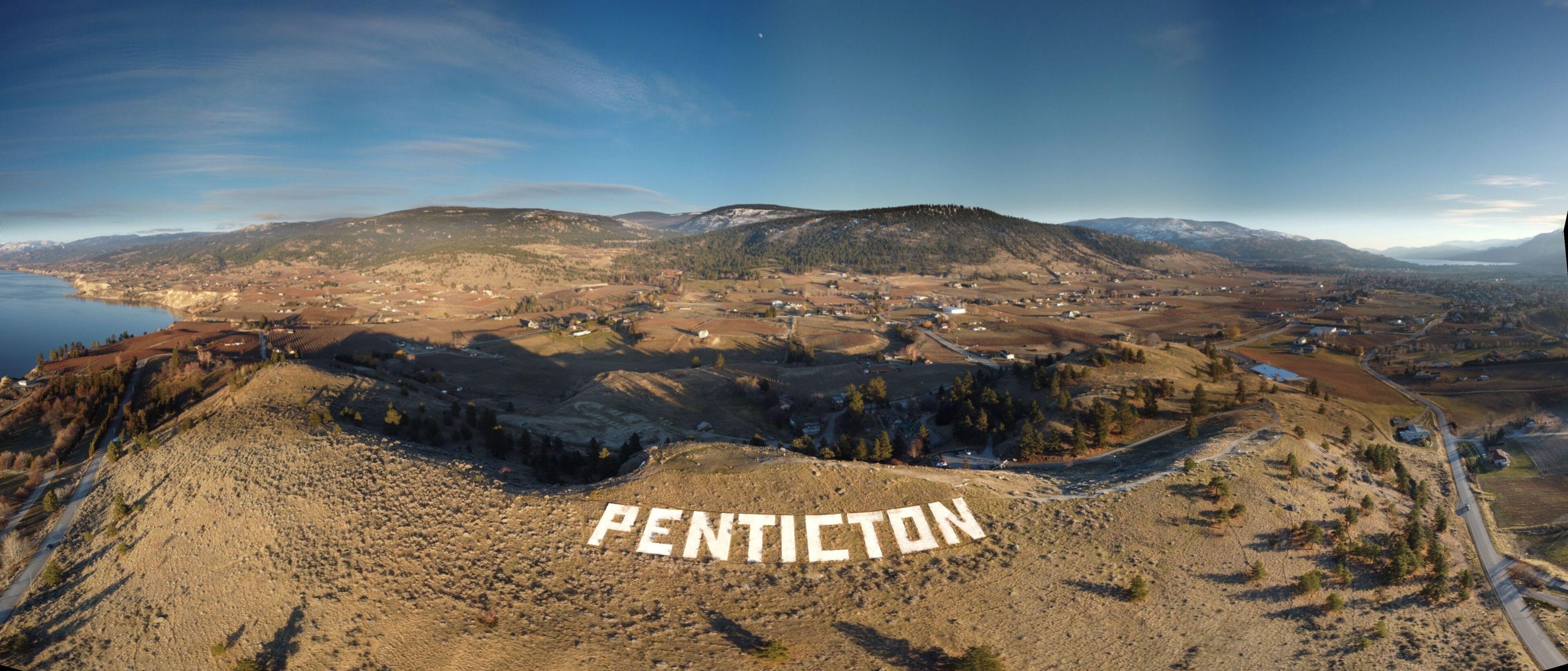 A panoramic view of Penticton, featuring a valley, mountains, and a river.