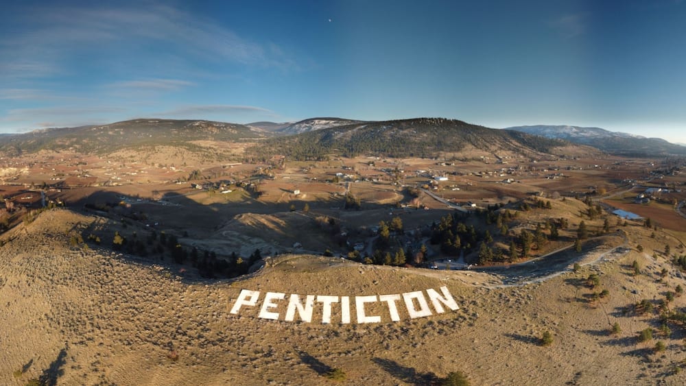 A panoramic view of Penticton, featuring a valley, mountains, and a river.