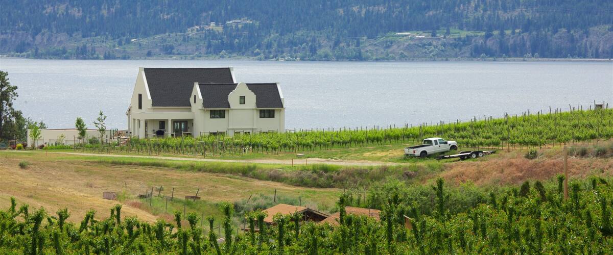 A house by a lake with vineyards and mountains in the background.