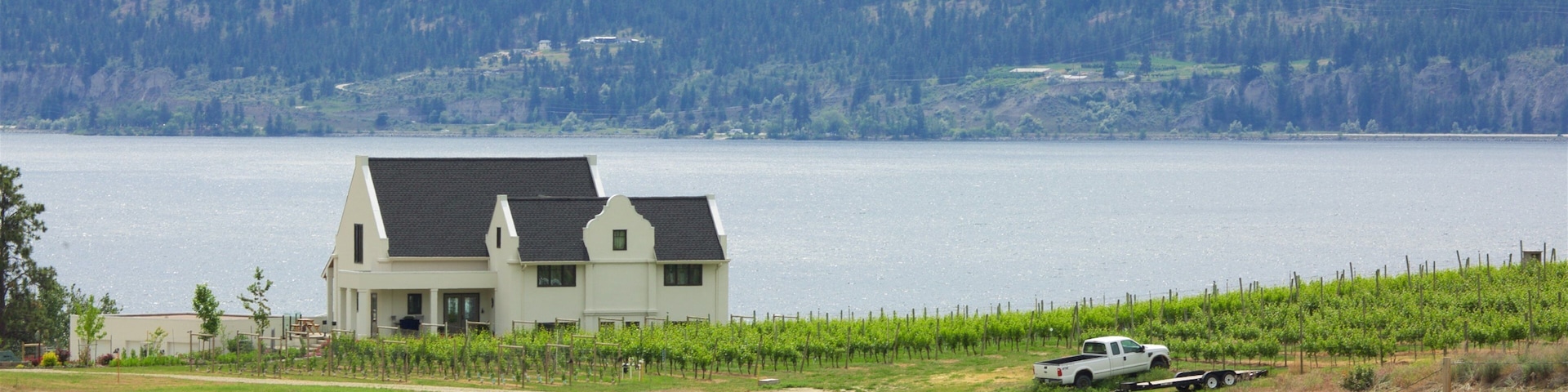 A house by a lake with vineyards and mountains in the background.