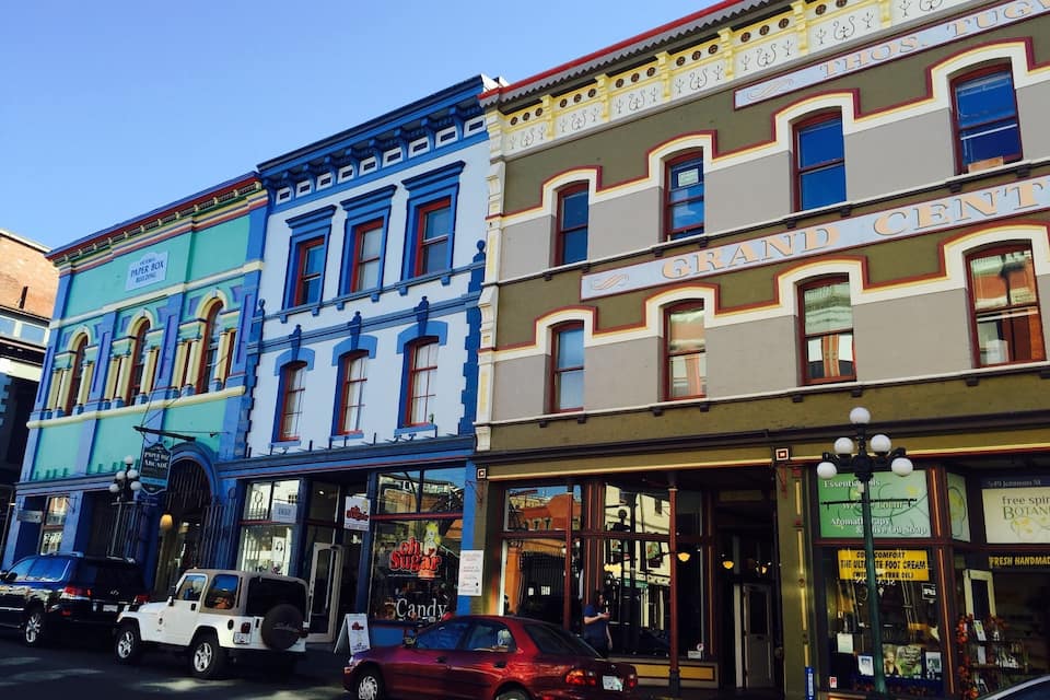 A street with colorful buildings, including a blue building with a sign for a paper box building and a brown building with a sign for Grand Central.