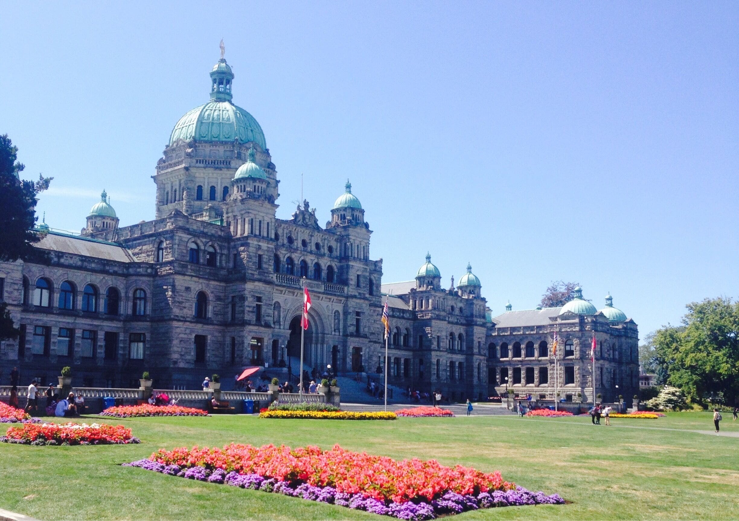 A grand historic building with multiple domes and flags, surrounded by vibrant flower beds.