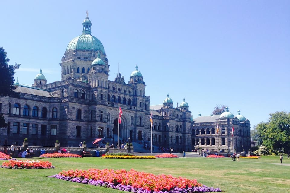 A grand historic building with multiple domes and flags, surrounded by vibrant flower beds.