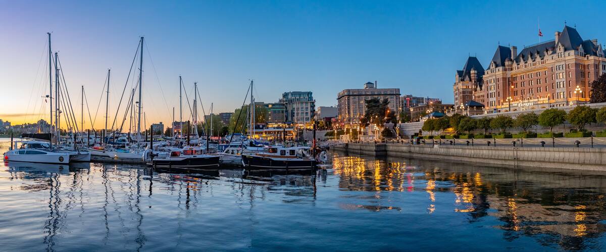 A marina with several sailboats docked, a waterfront promenade, and historic buildings in the background.