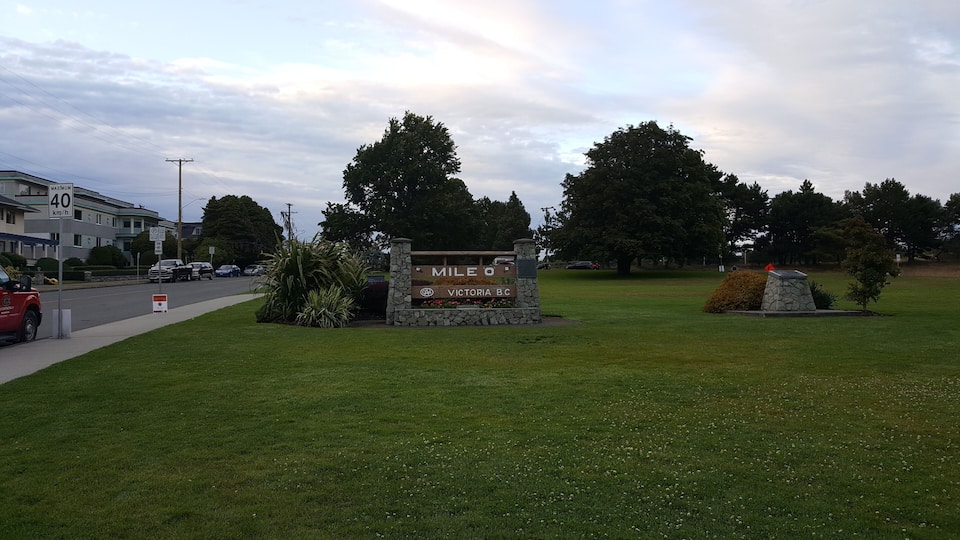 A sign for Mile 0 in Victoria, BC, surrounded by grass and trees.
