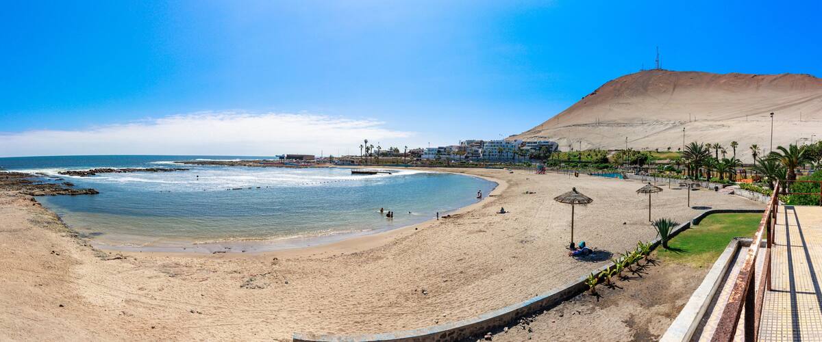 A beach with a sandy shore, a calm sea, and a large hill in the background.