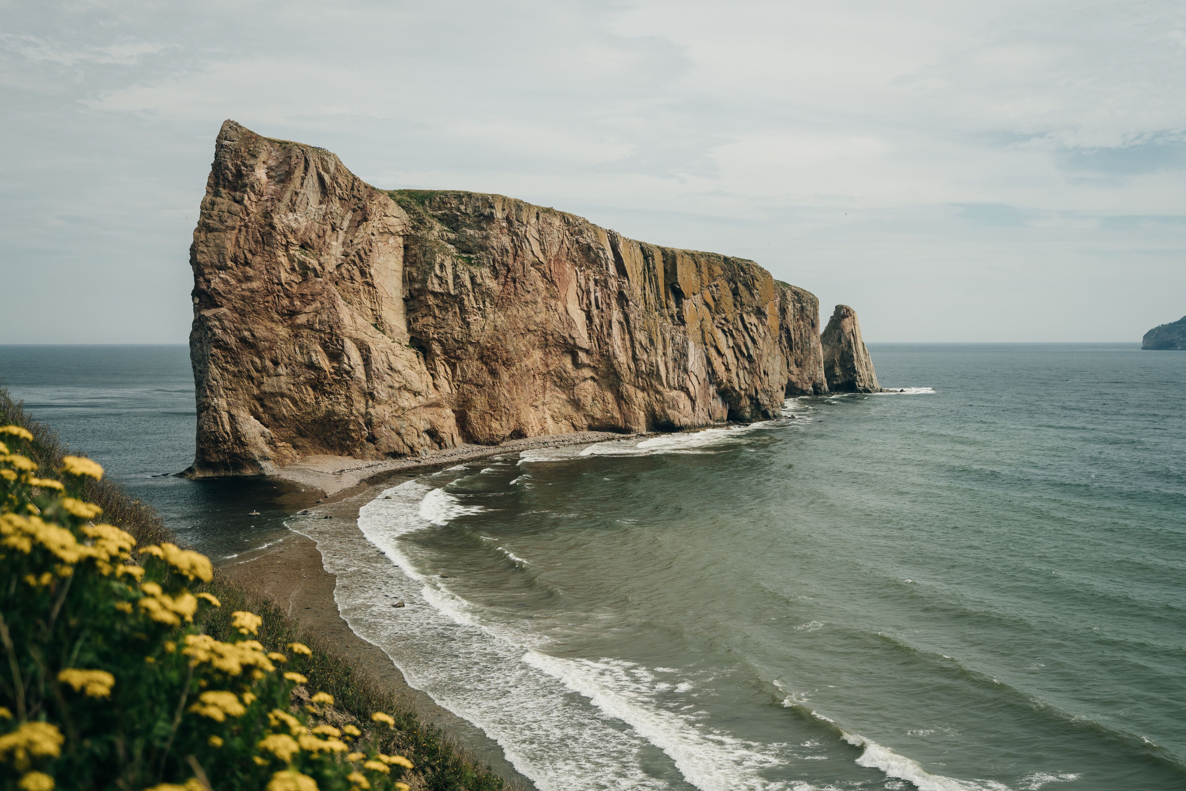 Une falaise côtière surmontée d’une formation rocheuse imposante qui s’avance dans la mer.