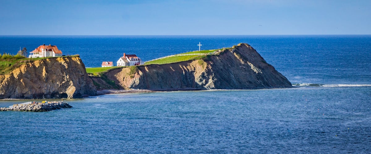A coastal landscape with a prominent cliff, a lighthouse, and several houses on the cliff edge.