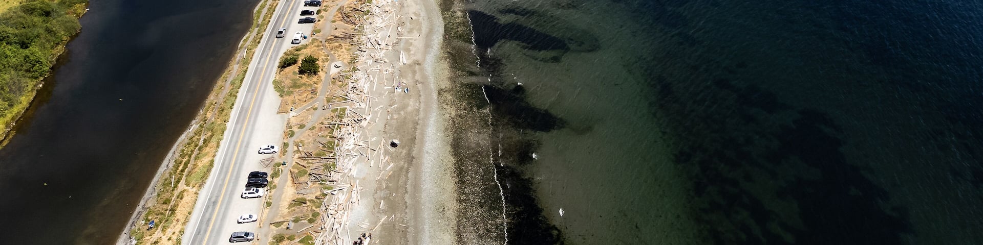 Aerial sand spit with a long straight road with people on vacation and cars parked in Victoria British Columbia Canada..