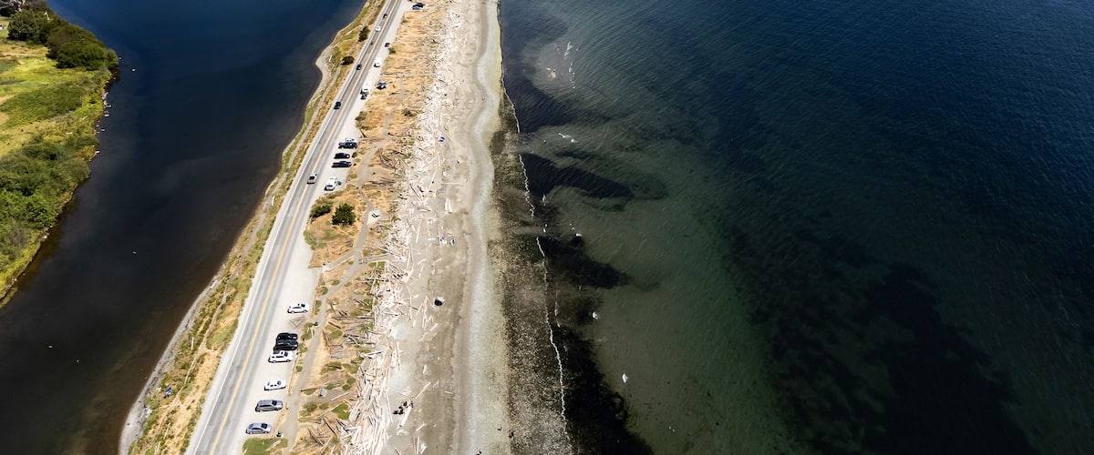 An aerial view of a coastal road with vehicles, a beach, and a large body of water.