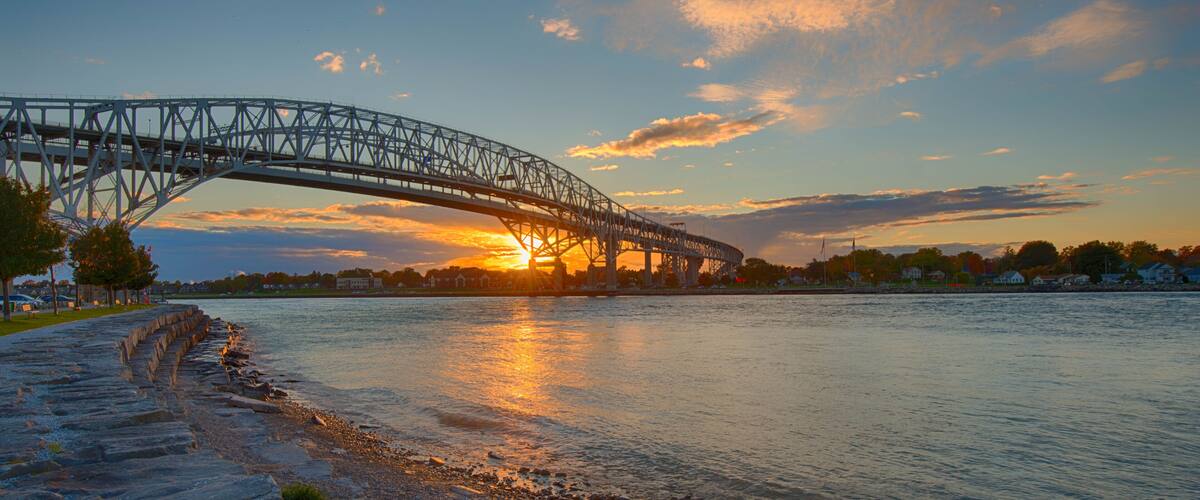 A steel bridge spanning a river with a sunset in the background.