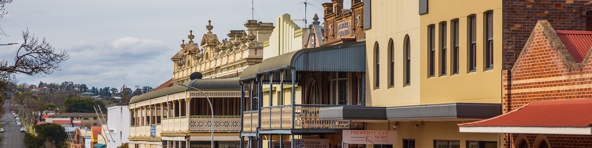 A street lined with historic buildings, including a prominent yellow building with a balcony and a brick building with a red roof.