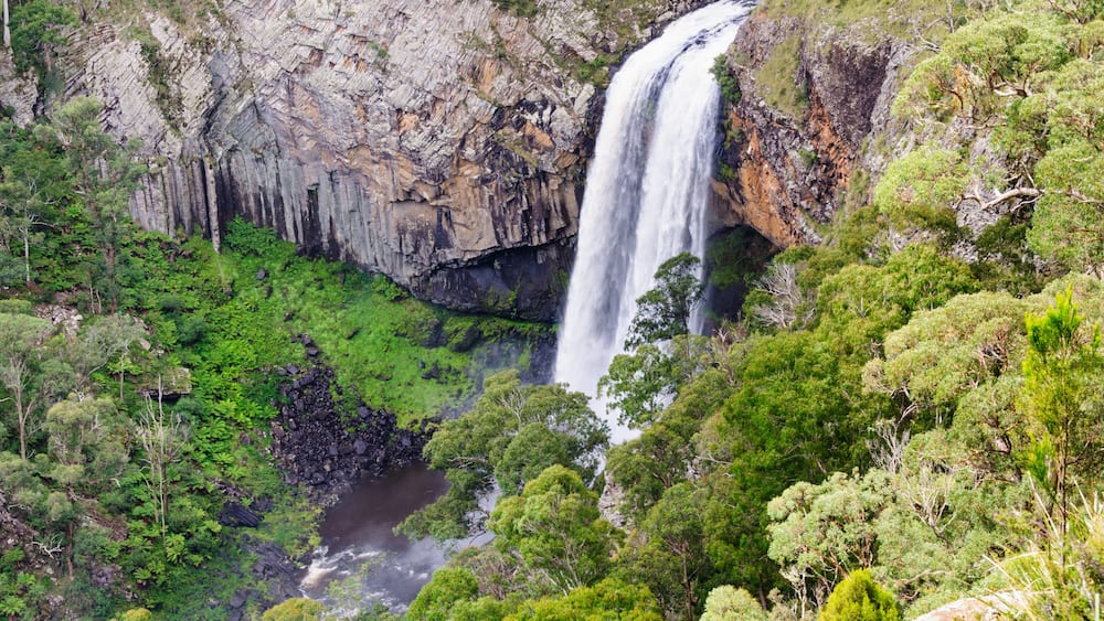 Ein Wasserfall stürzt über eine felsige Klippe, umgeben von üppigem Grün.