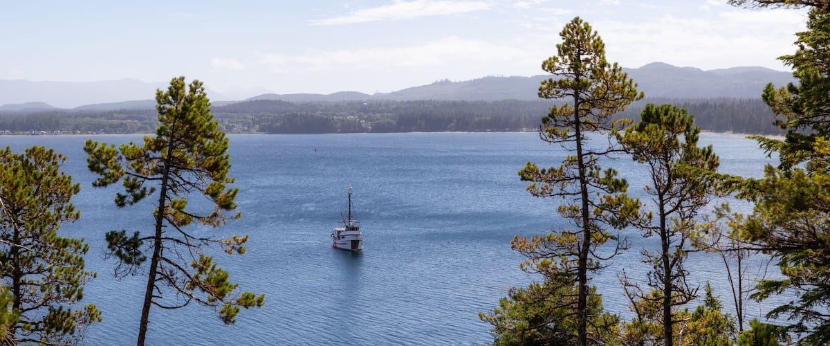A calm lake with a small boat, surrounded by evergreen trees and distant mountains.
