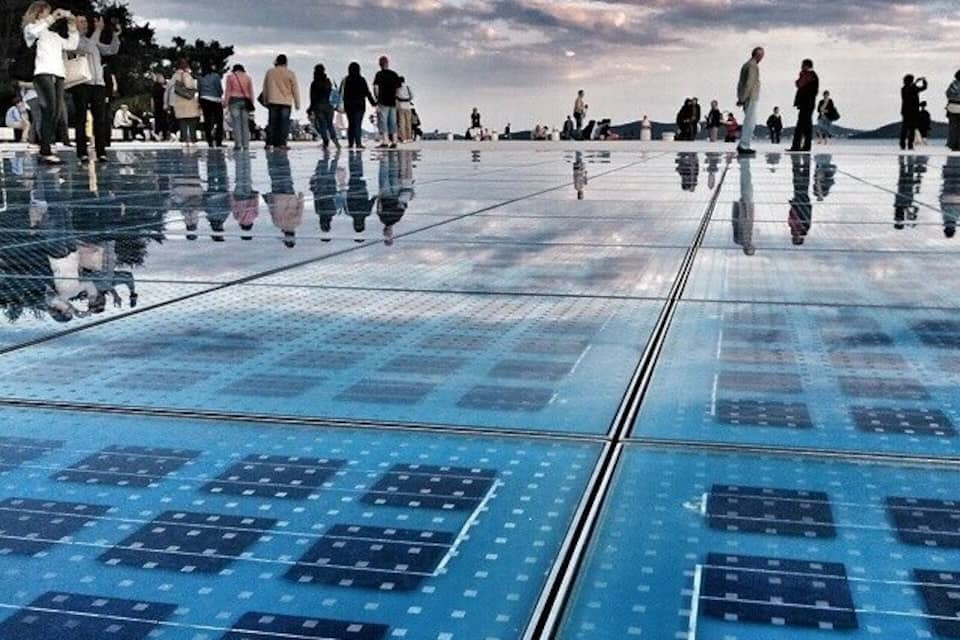A reflective glass floor with solar panels and people walking on it.