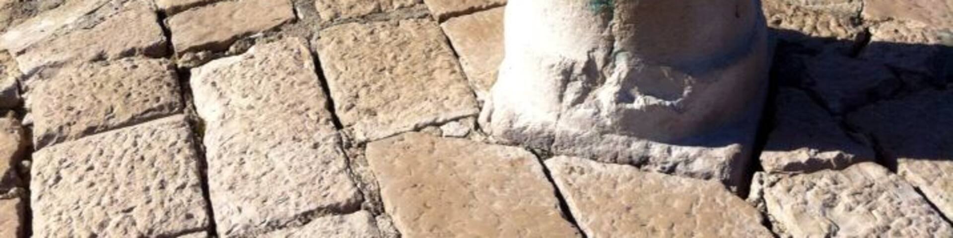 A stone pillar on a cobblestone path by the sea.