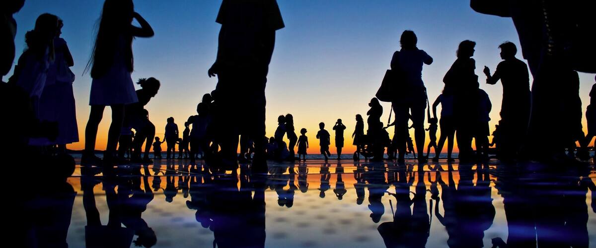 Silhouettes of people at a beach during sunset with reflections on the wet sand.