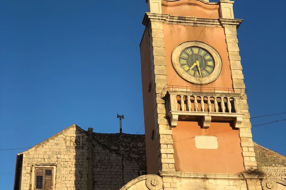A historic clock tower with a weather vane on top, set against a clear blue sky.
