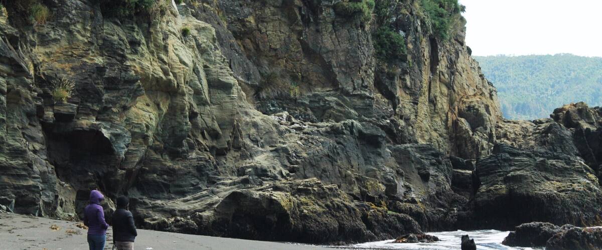 A rocky coastline with a cliff, beach, and ocean waves.