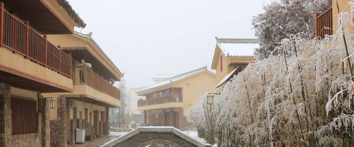 A snow-covered street with traditional buildings, a stone bridge, and a bamboo fence.