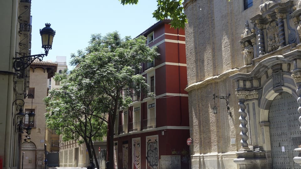 A narrow street with historic buildings, a tree, and a large ornate door.
