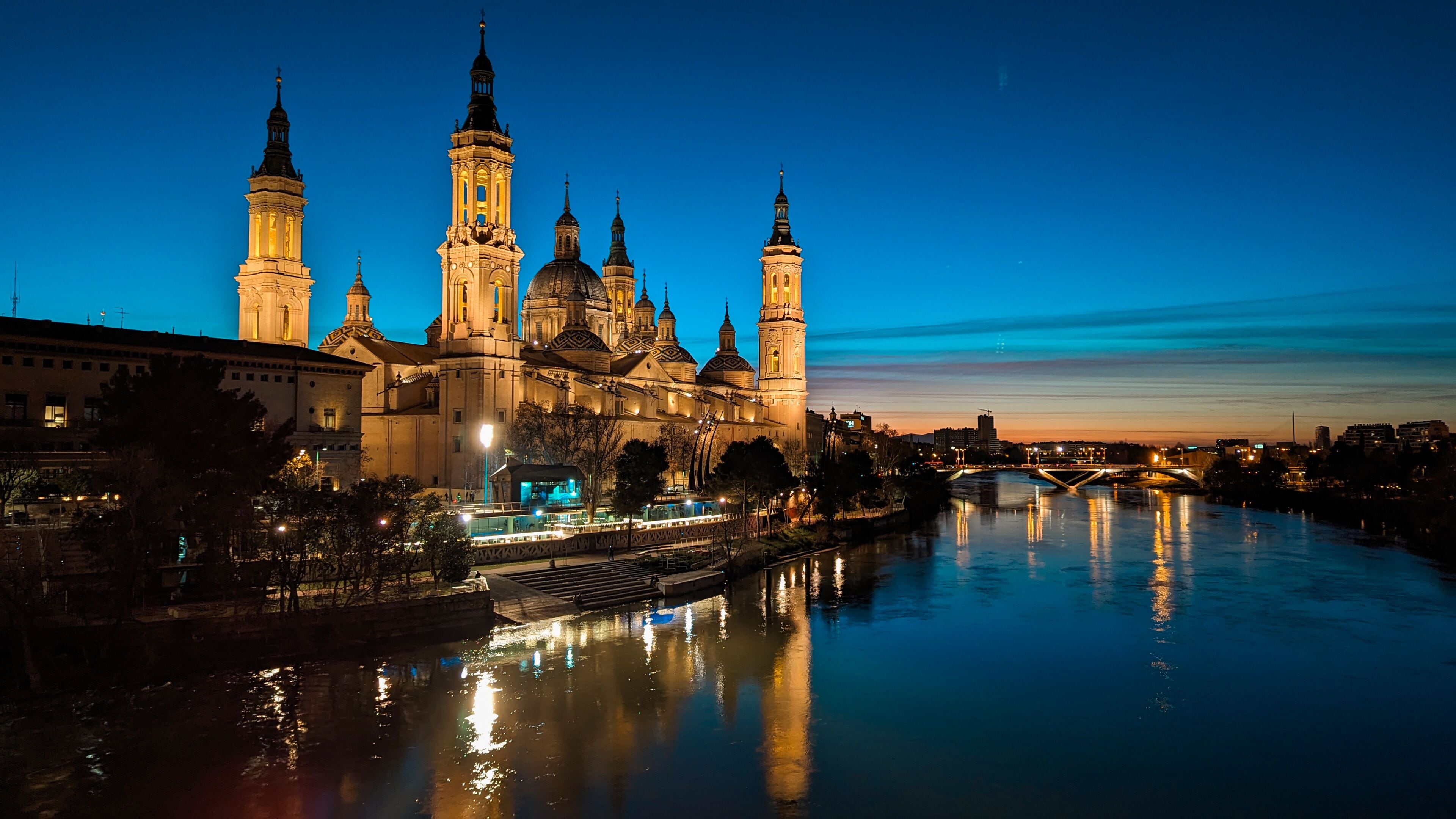 Beneath the Orange Sky, the Ethereal Silhouette of the Basilica of Our Lady of the Pillar Reflects in the Tranquil Waters of the Ebro River: A Magical Sunset in the City of Zaragoza