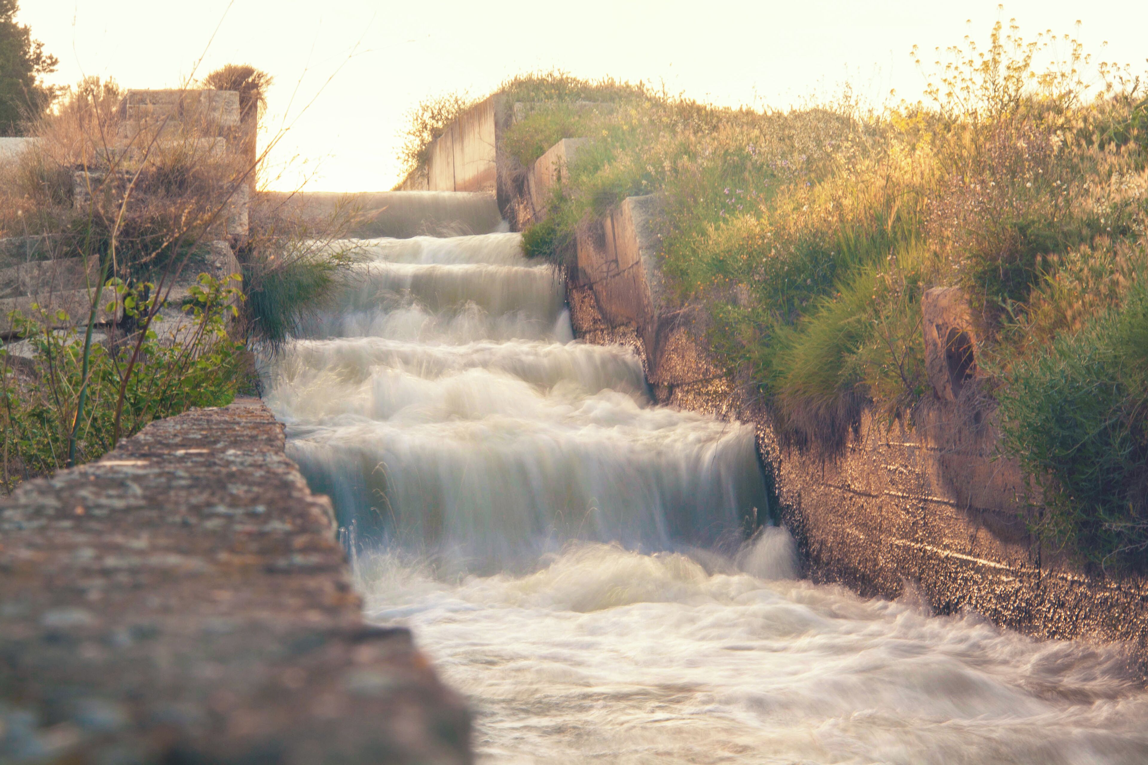A multi-tiered waterfall cascading over a stone structure surrounded by grassy terrain.