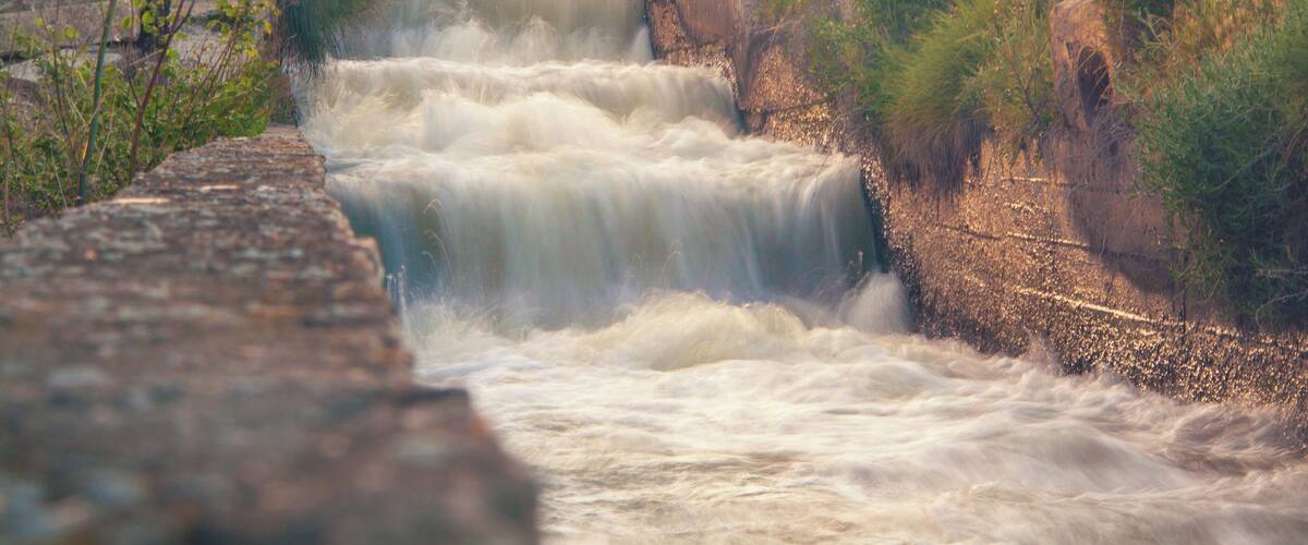 A multi-tiered waterfall cascading over a stone structure surrounded by grassy terrain.