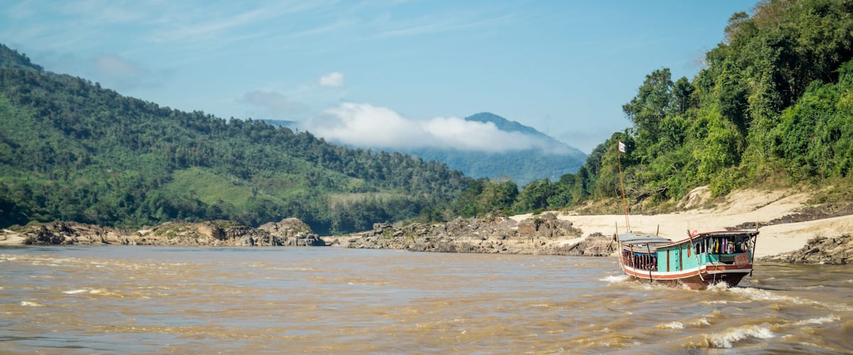 A boat on a river with a forested hillside in the background.