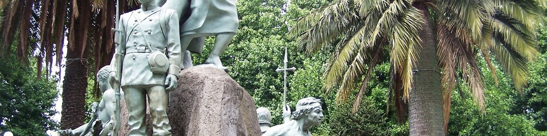Una estatua de un soldado y una mujer sobre una roca, rodeada de palmeras.