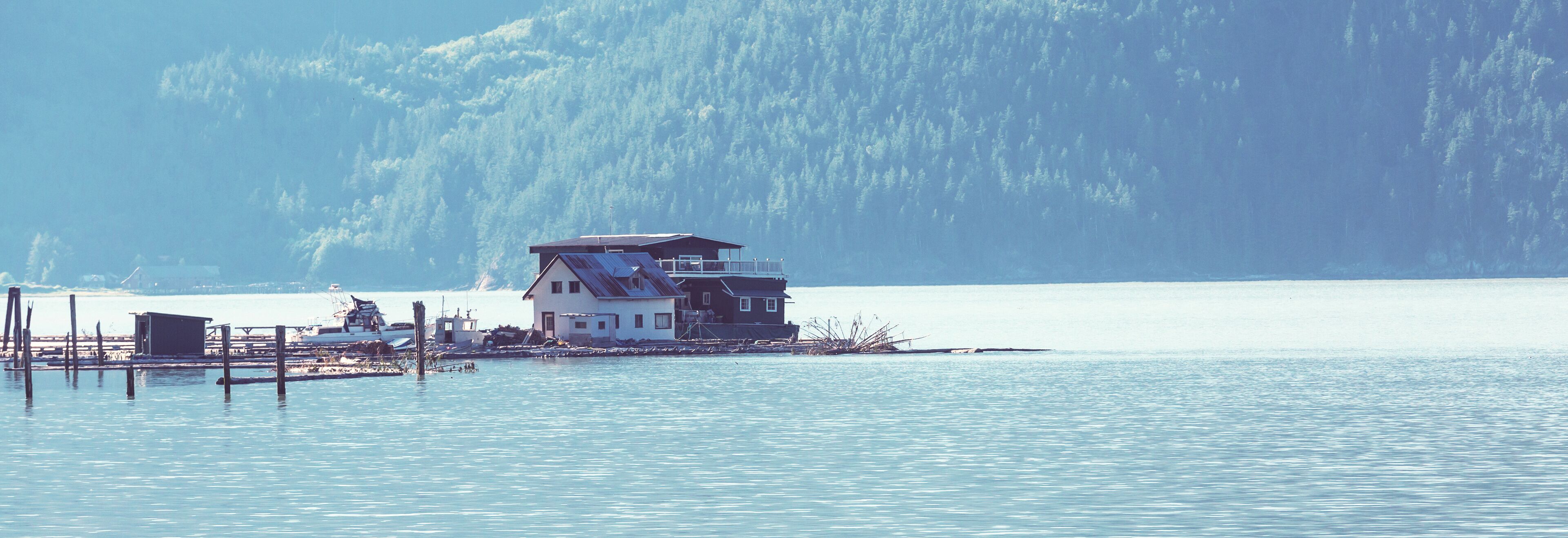 A house on stilts by a calm lake with a forest in the background.
