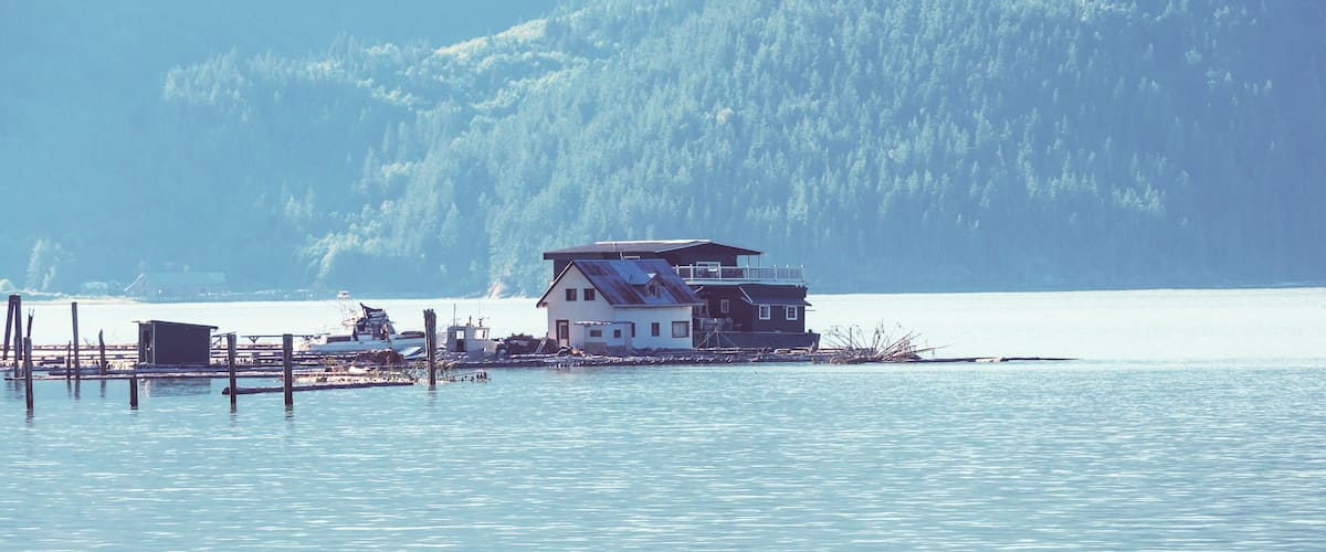 A house on stilts by a calm lake with a forest in the background.