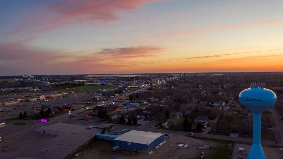 A sunset over a cityscape with a prominent blue water tower labeled "Watertown."