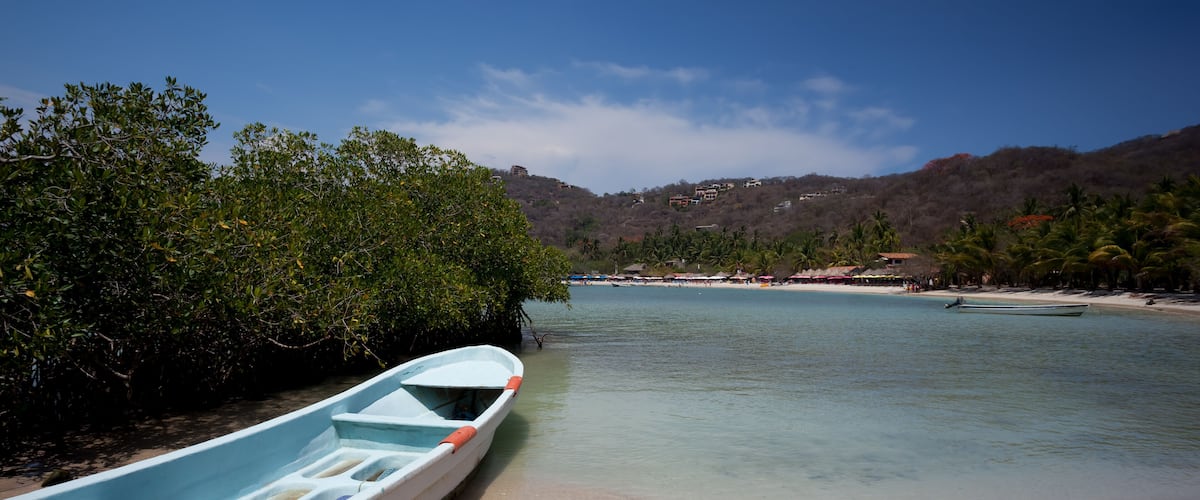 A calm river with a rowboat docked on the left, surrounded by lush greenery and a clear blue sky.