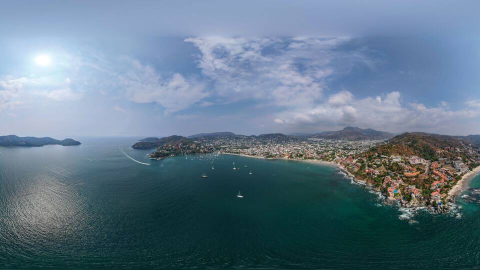 Una ciudad costera con una bahía, barcos y montañas al fondo.