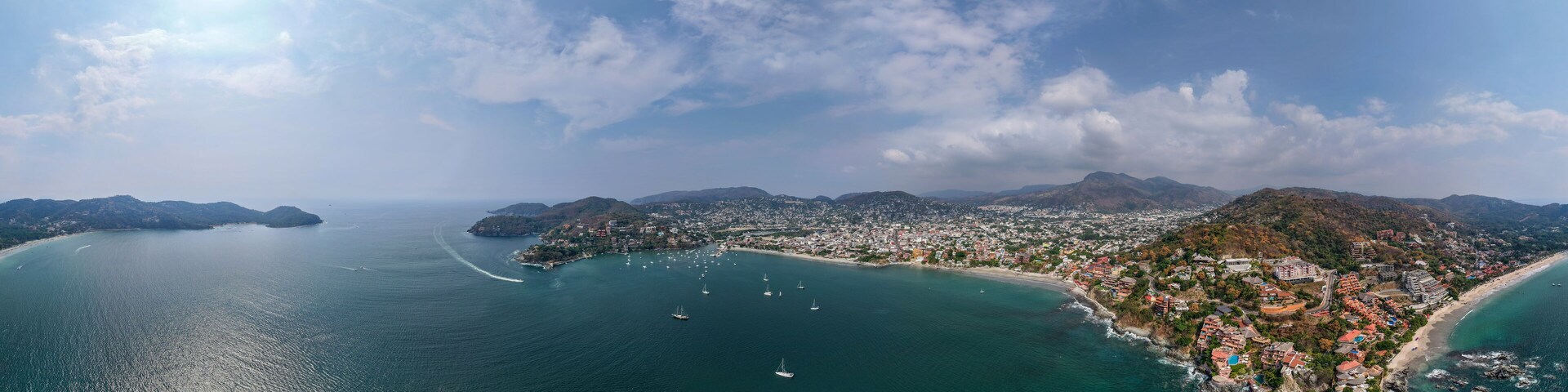 A coastal city with a bay, boats, and mountains in the background.
