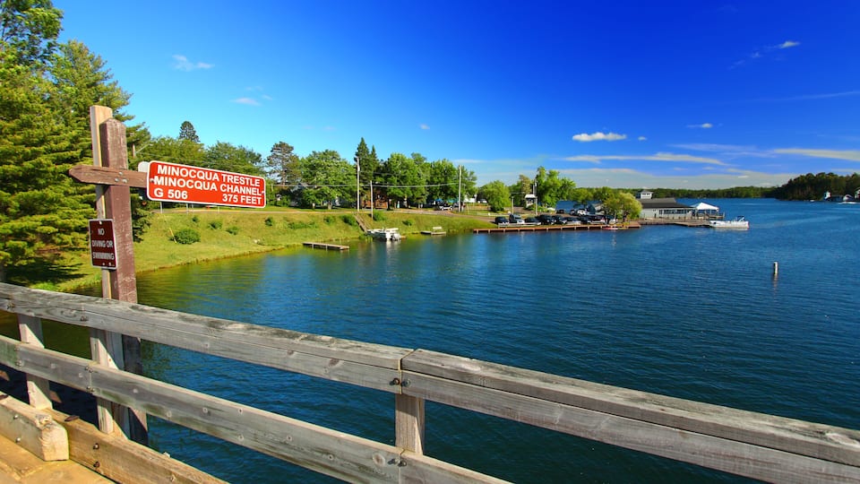 A wooden pier leading to a lake with a sign indicating the Minocqua Trestle Channel.