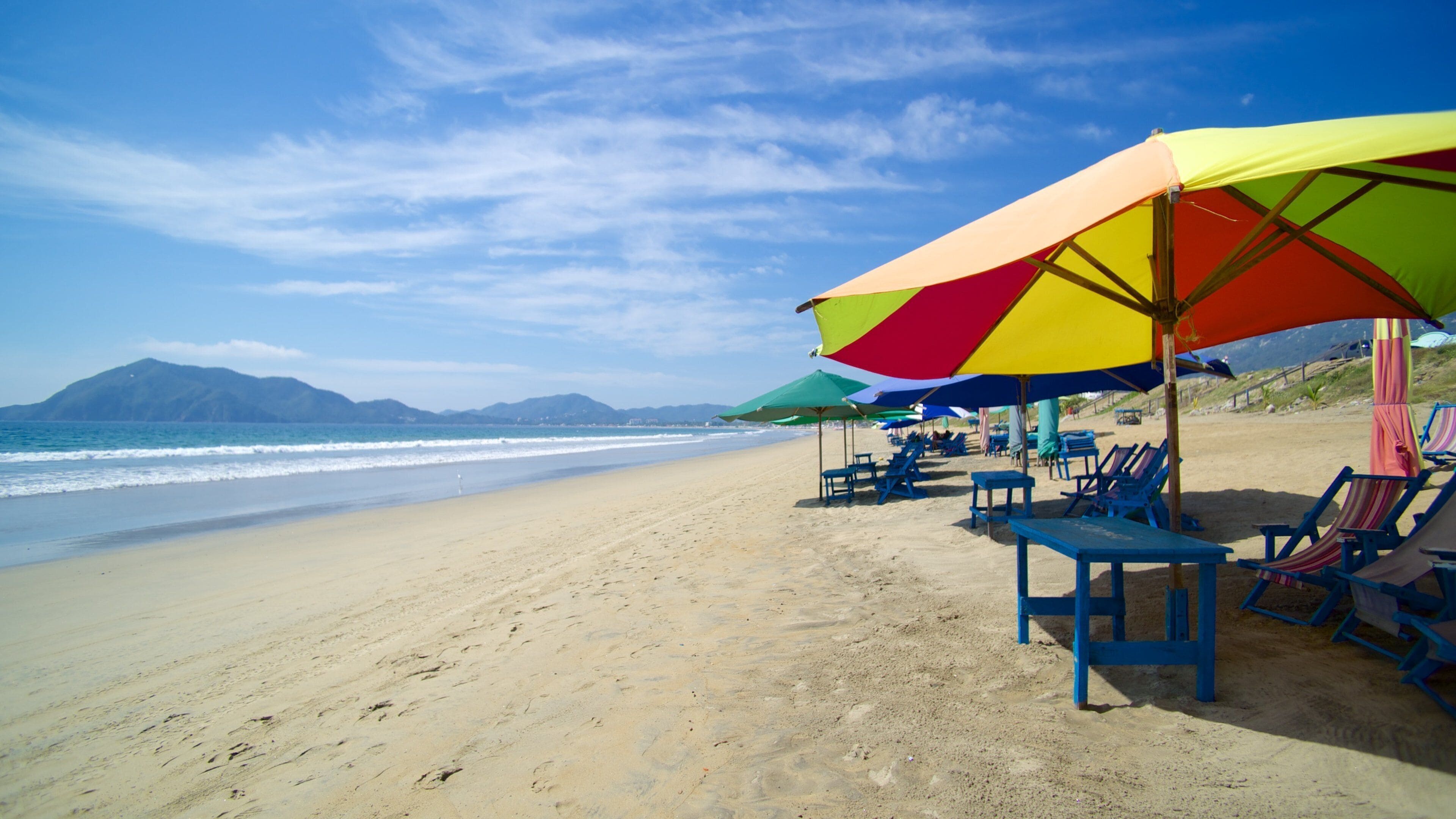 A beach with colorful umbrellas and blue lounge chairs.