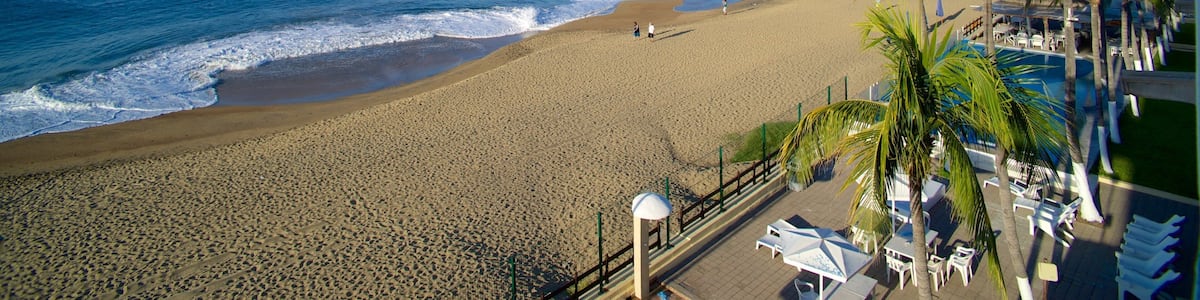 Une plage avec un navire visible au loin, des palmiers et une zone aménagée avec des chaises longues.