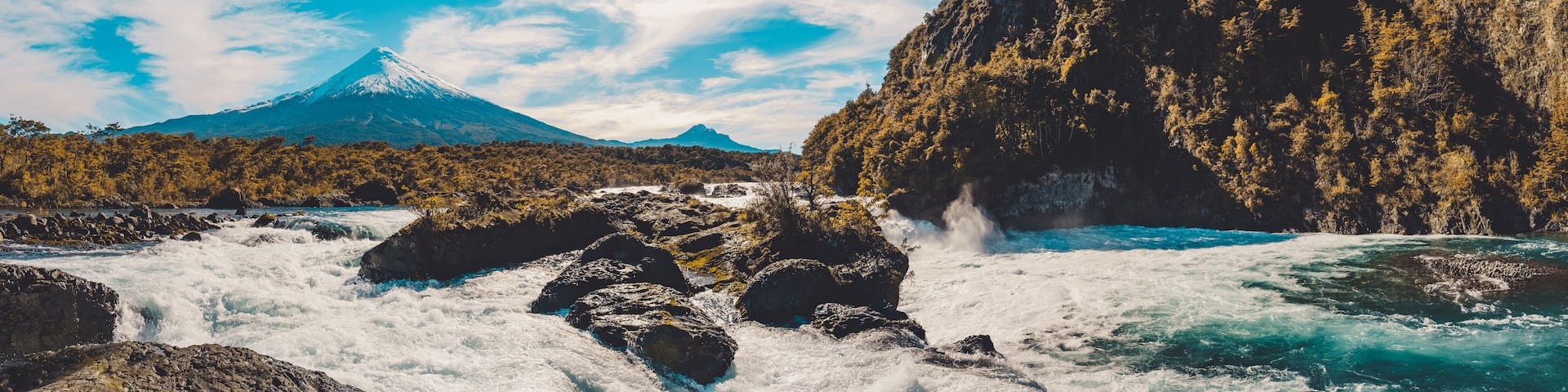 A river with white water rapids, a mountain with a snow-capped peak, and a forested area.