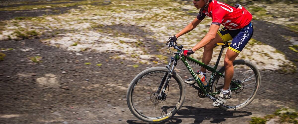 A cyclist on a mountain road with a snow-capped volcano in the background.