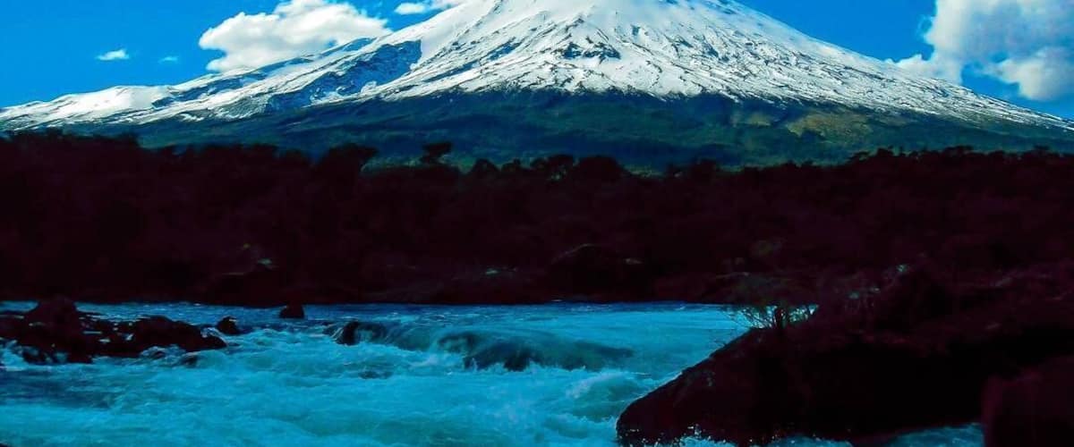 A snow-capped mountain with a river flowing in the foreground.